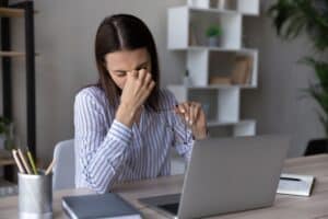 A woman pinching the bridge of her nose and closing her eyes while working on a computer